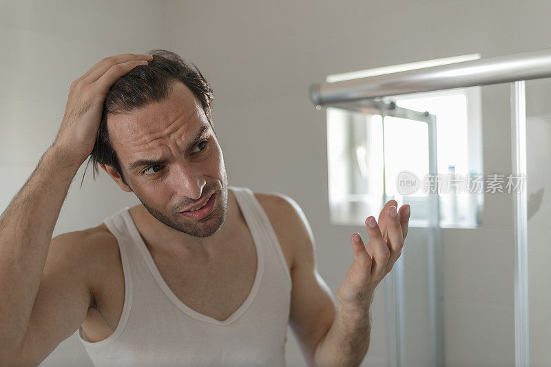一个年轻人看着浴室镜子里自己的头发