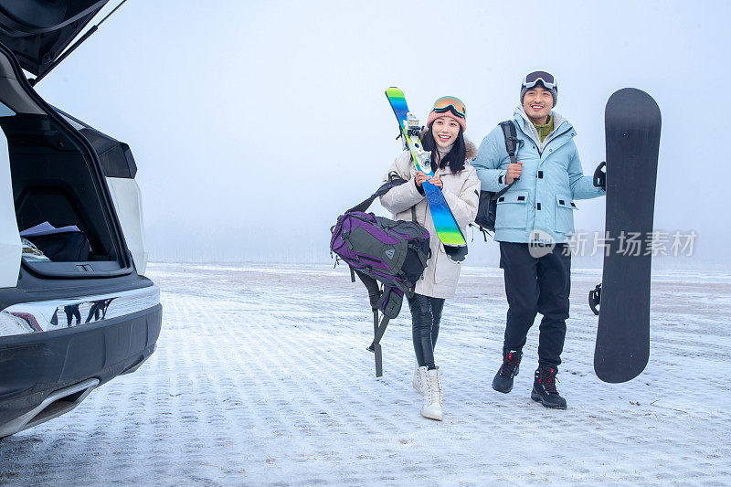 停车场上青年伴侣拿着滑雪板