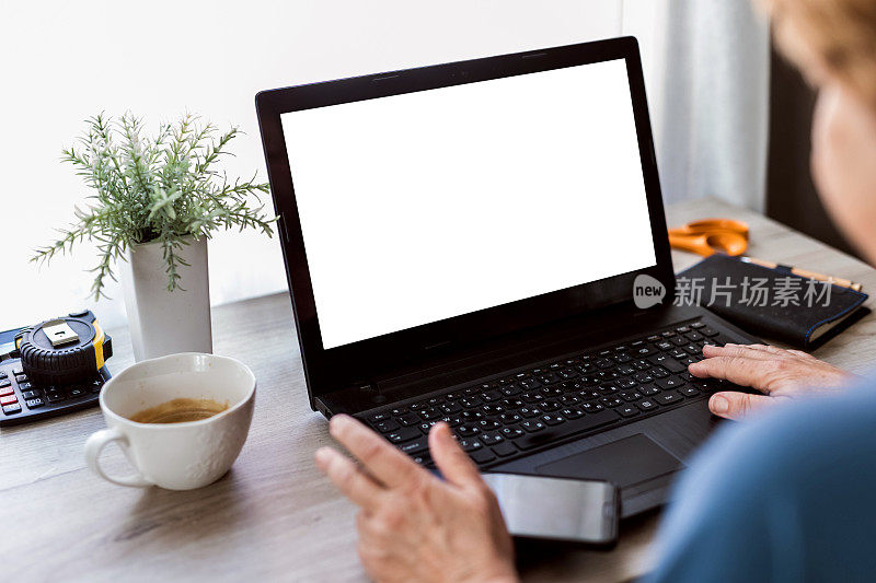 一位65-70岁的成熟女性在家办公时看着笔记本电脑的白色屏幕——库存照片