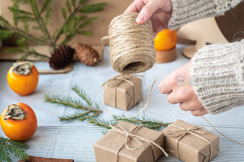 为圣诞节和新年包装时尚的现代礼物的过程。用牛皮纸、麻绳和圣诞树树枝做成的礼盒。圣诞背景，节日氛围