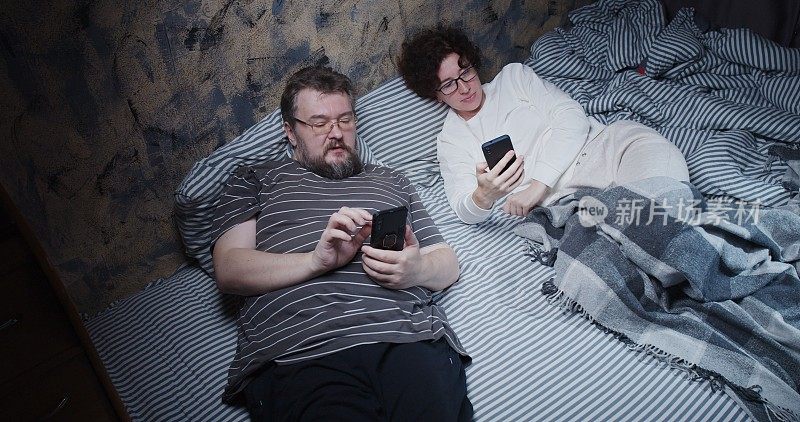 成熟的夫妻躺在床上，每个人都在用自己的智能手机交流
