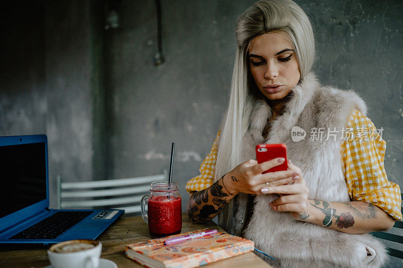 有纹身的女人在咖啡厅用笔记本电脑和智能手机