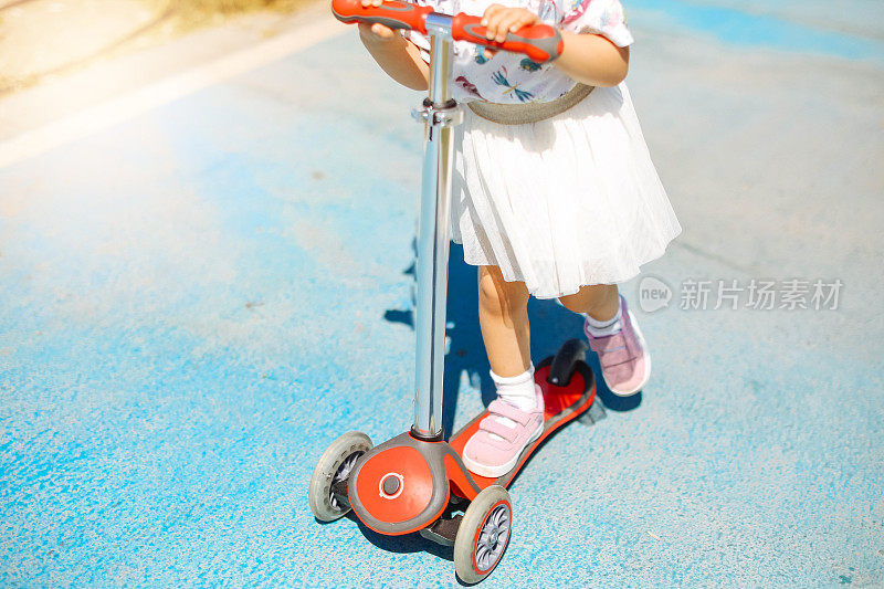 可爱的小女孩享受阳光明媚的一天，同时有一个推动滑板车的乐趣