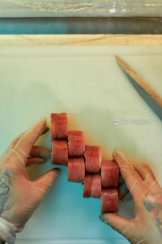 俯视图厨师安排金枪鱼寿司切片，同时准备在商业厨房的板上卷