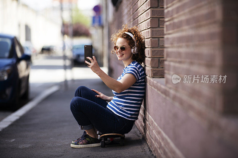 玩滑板的女孩用耳机打电话。库存图片