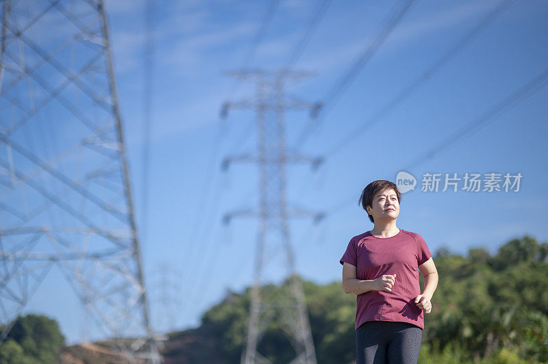 亚洲华人中年妇女与运动服跑步在早上与电力线蓝色的天空背景
