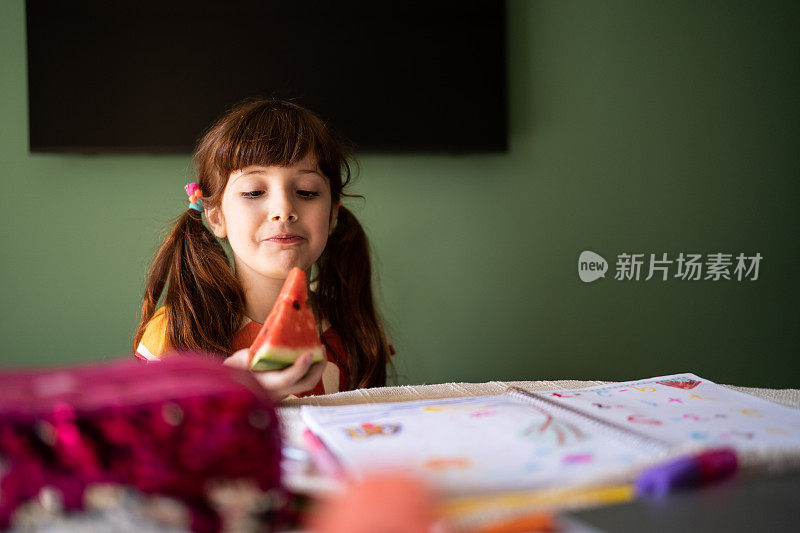 可爱的女孩一边在家学习一边吃着西瓜片