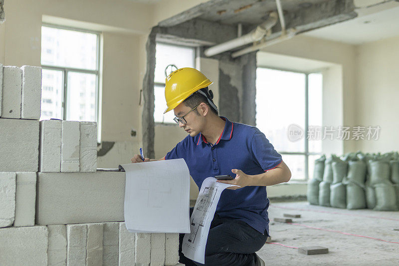 亚洲男性工程师，在装修工地处理建筑图纸和手机