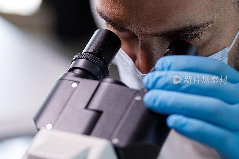 男性科学家在显微镜下观察病毒样本的照片