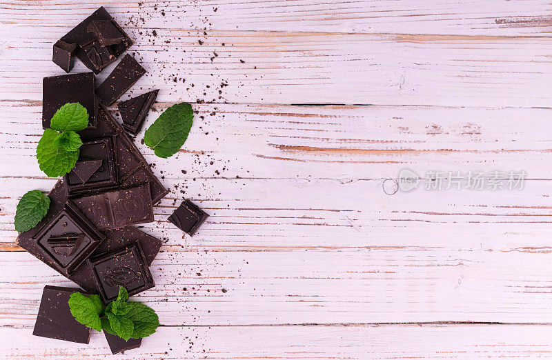苦黑巧克力片，绿色薄荷，白色木制背景。平的花环。副本的空间。