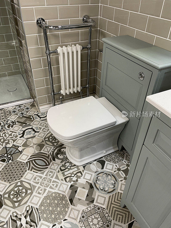 现代浴室的形象与白色，方形卫生间水箱隐藏在灰色梳妆台，铬毛巾栏杆散热器挂在墙上的光滑瓷砖，棕色瓷砖，独立淋浴间，有图案的地砖