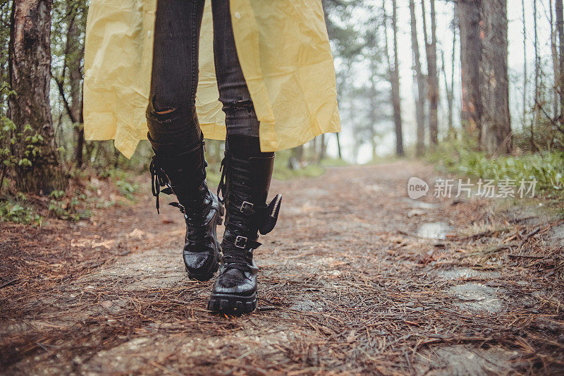 一个快乐的年轻女子在一个下雨天穿着一件黄色雨衣在树林里享受大自然。