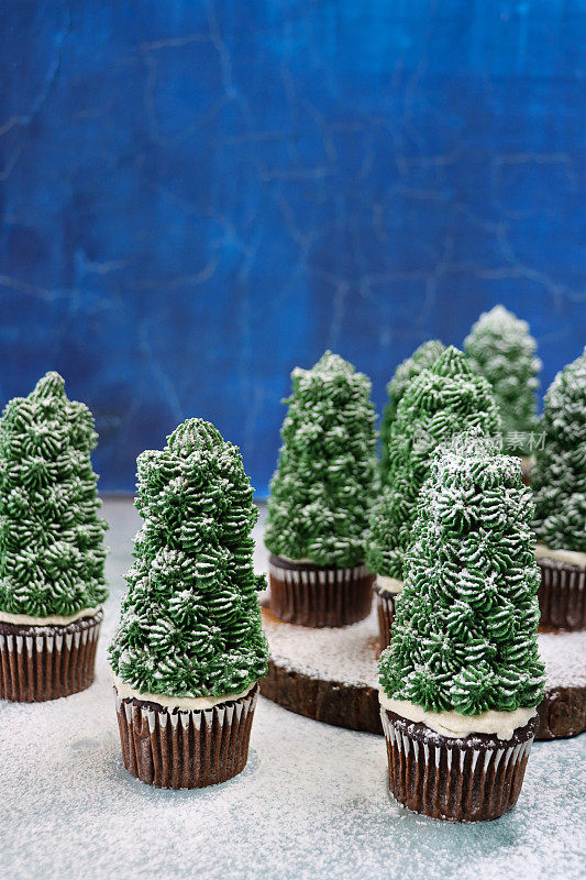 图像批量自制，圣诞树设计的巧克力纸杯蛋糕在纸蛋糕盒展示在蛋糕架在雪，夜晚针叶林的场景，重点前景