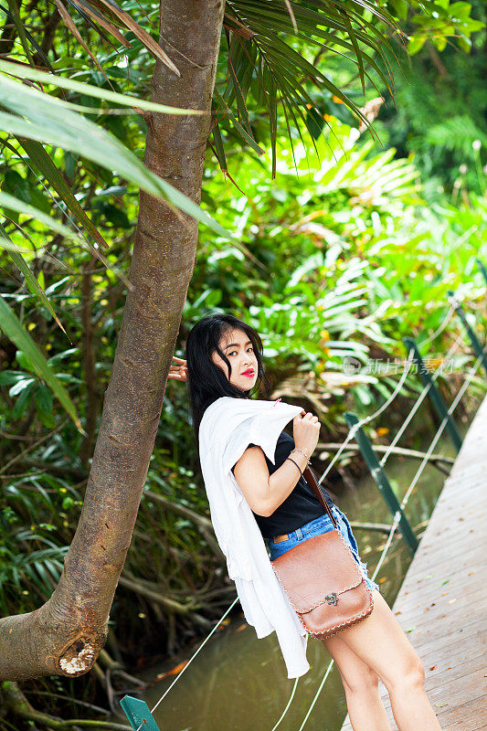 泰国女孩拿着包在公园的木板路上