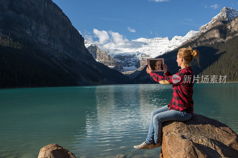 一名女子在湖边用平板电脑拍摄风景