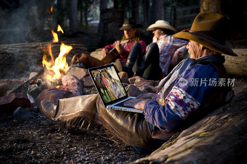 老牛仔围着篝火在笔记本电脑上编辑照片
