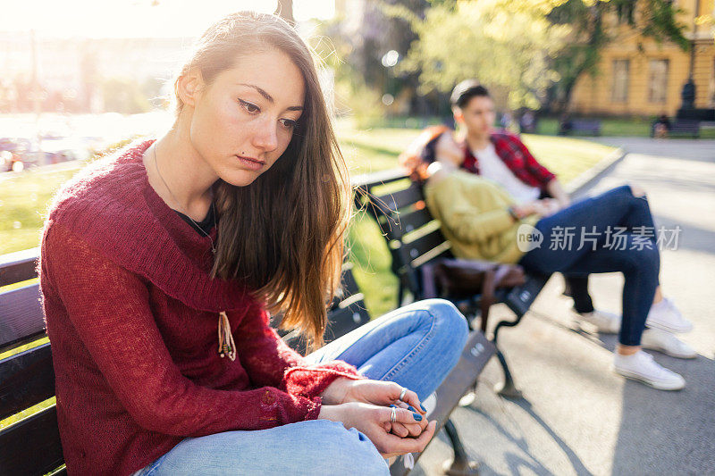 孤独的女孩因为隔壁长椅上的一对幸福的情侣而伤心