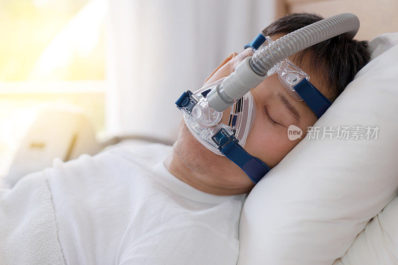 睡眠呼吸暂停治疗，男人戴着呼吸面罩睡在床上。