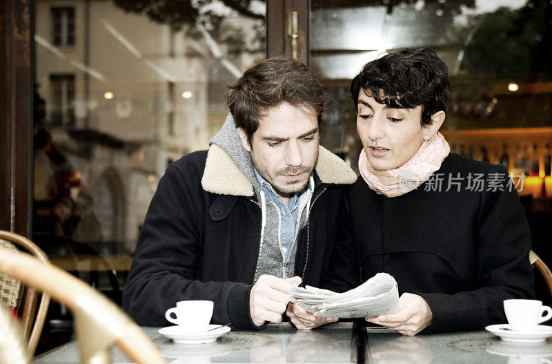 一对年轻夫妇在咖啡馆里看报纸