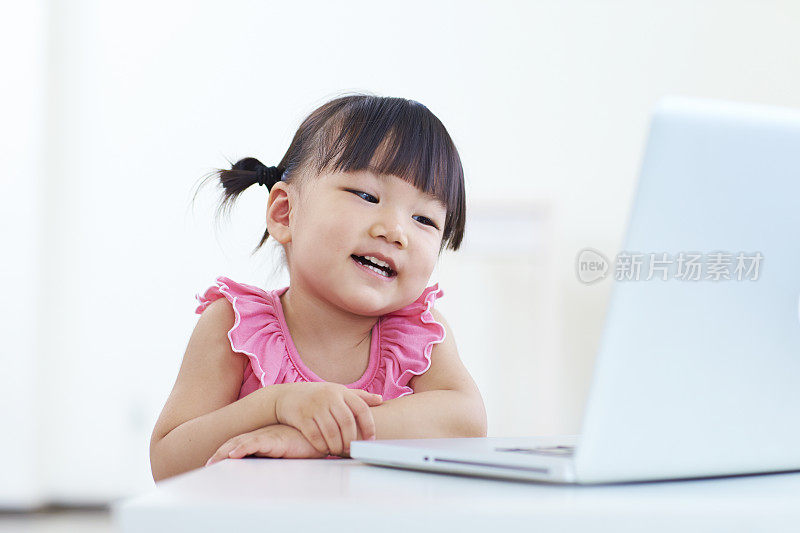 可爱的亚洲小女孩在室内使用笔记本电脑
