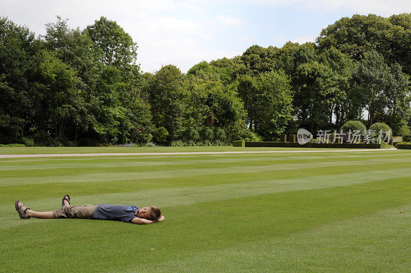 懒洋洋地打哈欠的男孩躺在公园的草地上