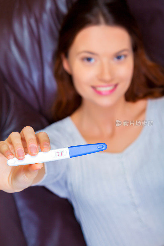 年轻女子微笑着，在室内展示怀孕测试的阳性结果