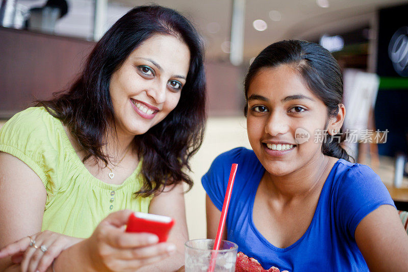 快乐的印度母亲和女儿在食堂发送阅读短信