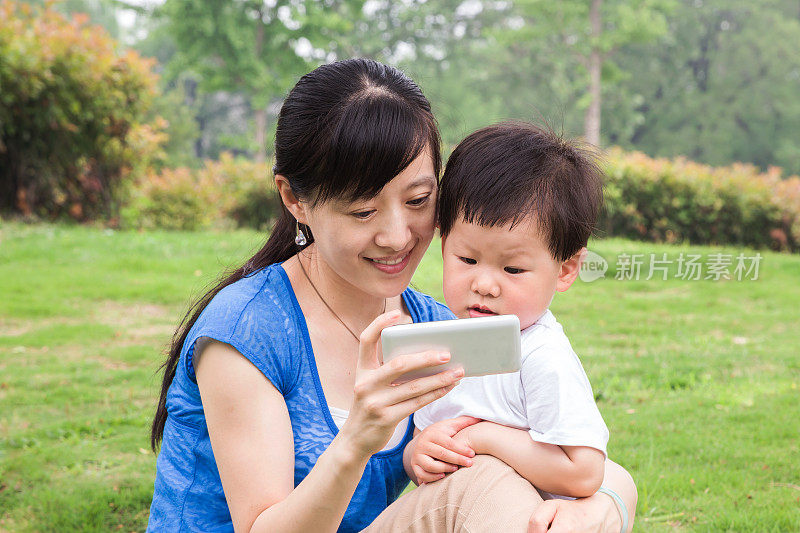 亚洲母亲和婴儿在草地上使用手机