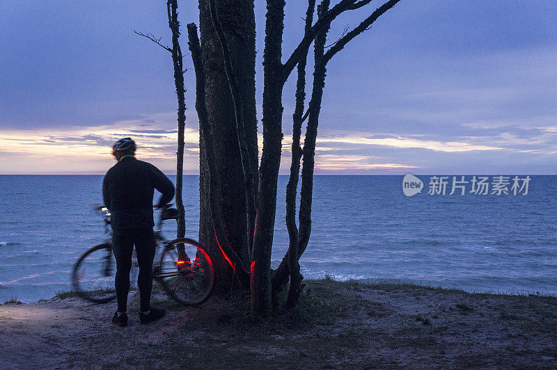 成熟的男人骑着自行车沿着海边旅行，黄昏时分