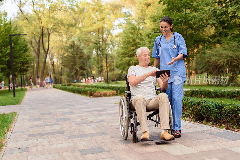 一位坐在轮椅上的老人向护士展示平板电脑上的东西