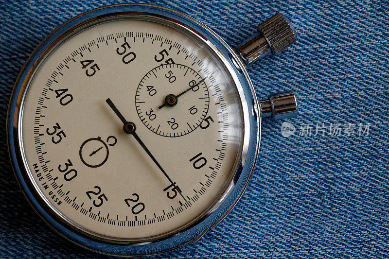秒表在破旧的蓝色牛仔裤的背景下，值测量时间，旧时钟箭头分秒精确计时器记录