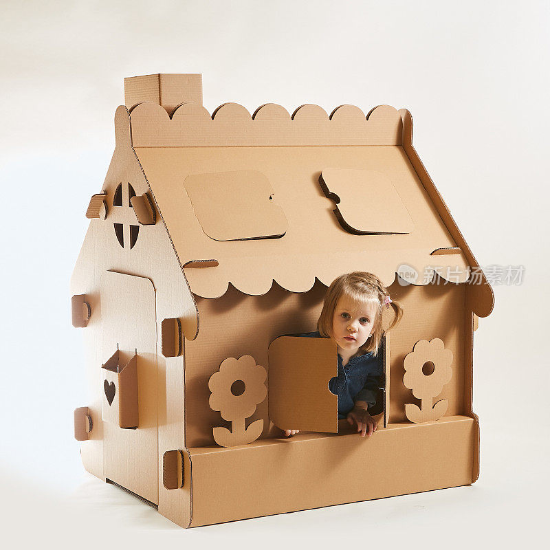 一个小女孩在纸板房子里玩。幸福的概念，人，家庭，孩子，童年，在幼儿园或在家里玩