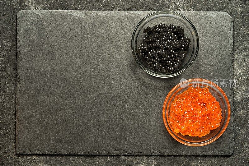 红鲑鱼籽和黑鲟鱼子酱放在黑色的桌子上的黑色石头板上，顶视图与拷贝空间。