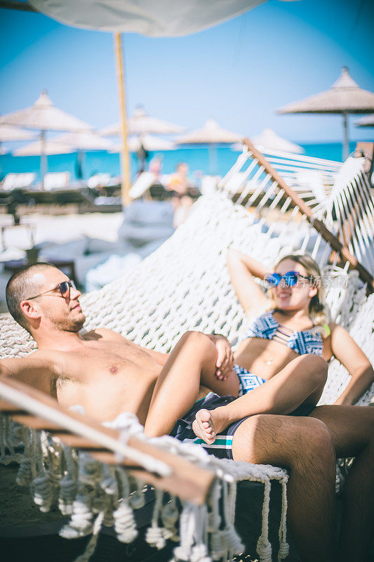 一对浪漫的年轻夫妇在热带海滩的吊床上放松