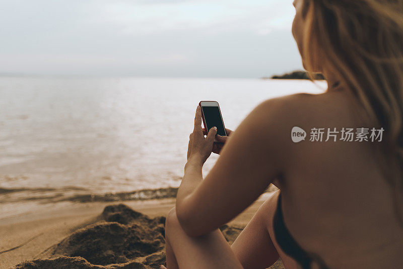 一个年轻女子在海滩上使用手机的特写
