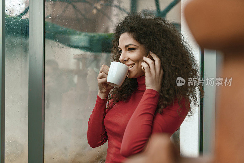 漂亮的年轻女子一边喝咖啡一边玩智能手机