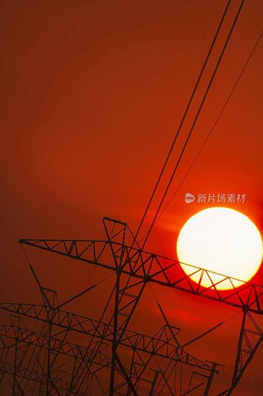 炎炎夏日，太阳落在一排高压输电塔后面