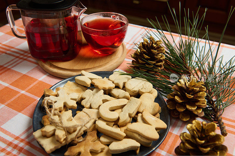 圣诞节的静物画。姜饼饼干，茶壶和茶杯，芙蓉茶，冷杉树枝，金色松果放在桌子上