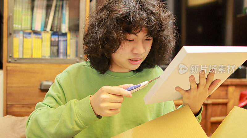 一个亚洲少年正在打开网上订购的快递包裹