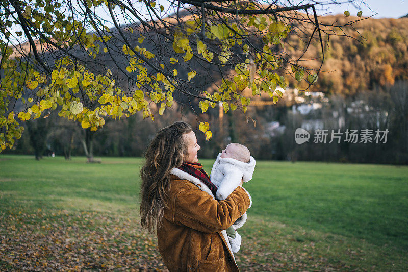 妈妈抱着女儿穿过湖边公园