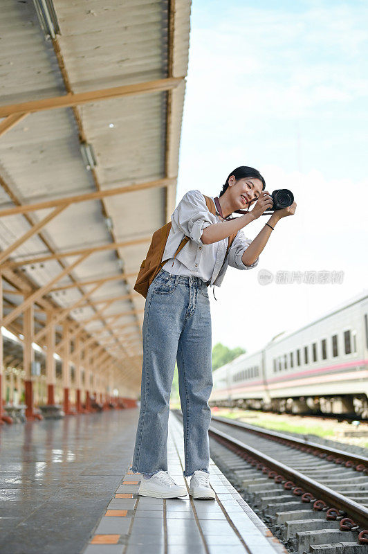 一位女背包客在火车站用相机拍照。