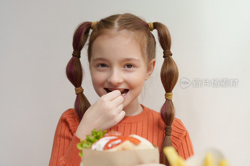 快乐的白人女孩扎着马尾辫，笑着吃着陀螺。快乐的孩子在餐厅享受希腊快餐餐