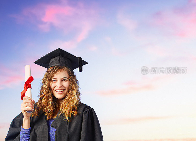 美丽快乐的年轻女子穿着毕业礼服和学位帽，映衬着明亮的夏日天空