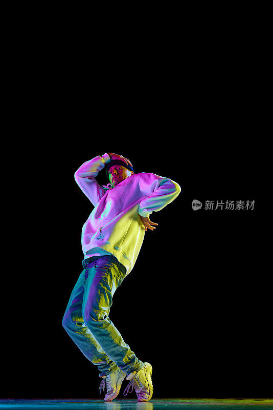 年轻时尚的男子，霹雳舞舞者，在舞厅里，在粉红色霓虹灯的黑色背景下，穿着休闲装独自练习。