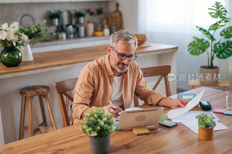 一个男人坐在舒适的家里，看着笔记本电脑，处理文书工作，解决家庭财务问题。