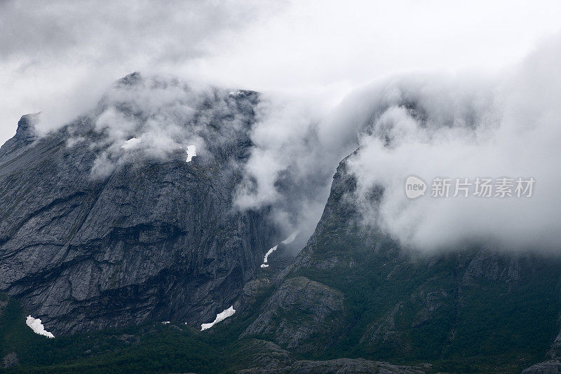 云层层叠在挪威崎岖的悬崖上，在持久的石头上创造了一个戏剧性的光影相互作用，这是一个自然的画布，自然的力量在发挥作用