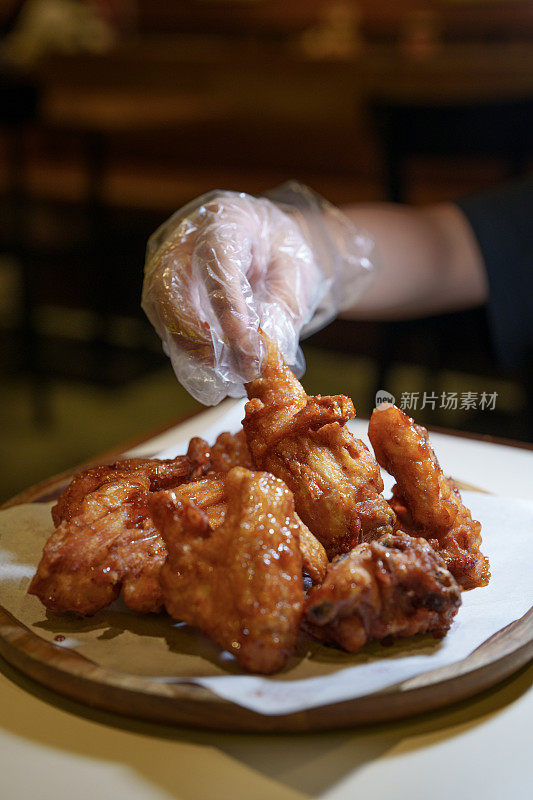 在这张裁剪过的图片中，一个戴着塑料手套的人的手拿着一家餐馆里的韩国炸鸡。