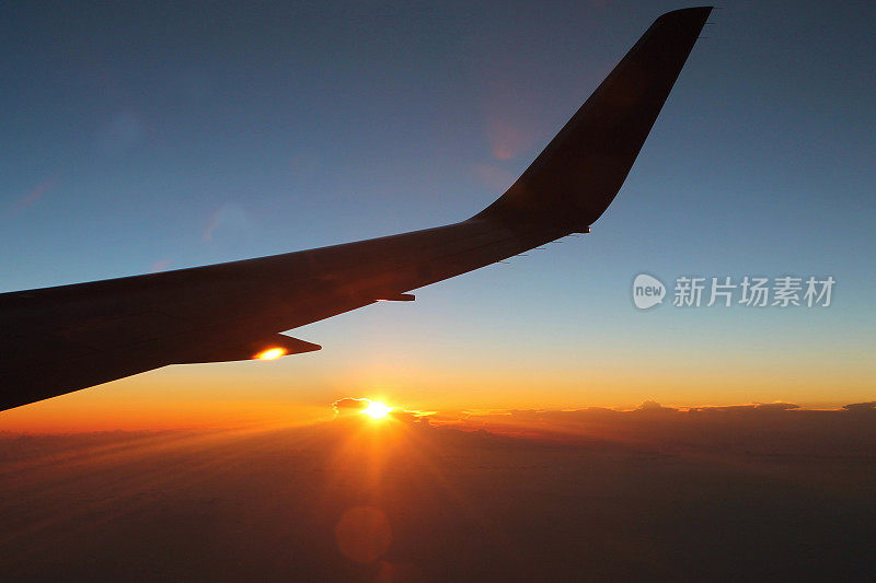 日出时从飞机窗口看到的景象。飞机的翅膀，湛蓝的天空和太阳升起的背景。