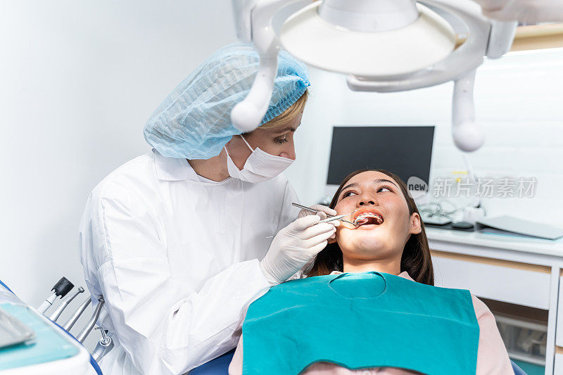正畸医生在牙科诊所为女病人检查牙齿。漂亮的年轻女孩戴着牙套躺在牙科椅上，在医院的牙科服务期间接受牙医的牙科治疗