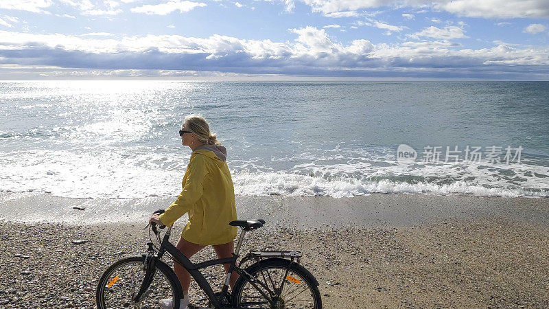 成熟的女人推着自行车沿着空旷的海滩